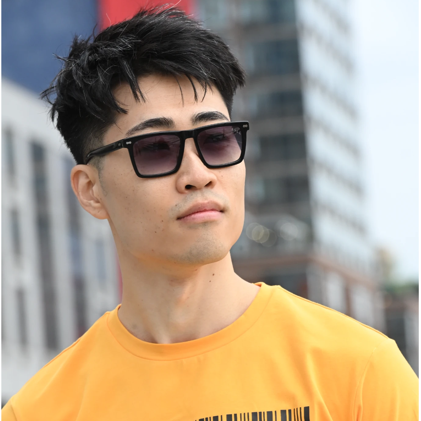 Man wearing sunglasses and a bright orange t-shirt with a barcode design, standing outdoors.